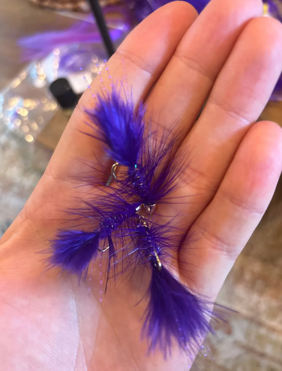 Three hand-tied purple Woolly Buggers held in an open palm at the vise.